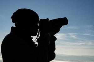 silhouette di giovane fotografo che tiene una macchina fotografica con paesaggio di montagna foto