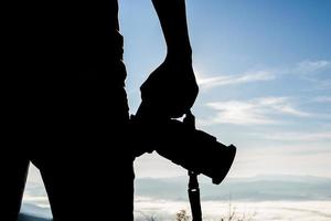 silhouette di giovane fotografo che tiene una macchina fotografica con paesaggio di montagna foto