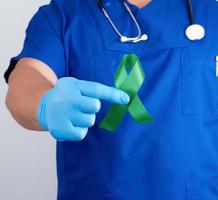 medico nel blu uniforme e latice guanti detiene un' verde nastro foto