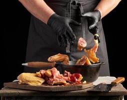 capocuoco nel nero uniforme e latice guanti chopping lanci affettato pollo in un' nero ghisa frittura padella foto
