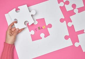 femmina mano mette bianca grande puzzle su un' rosa sfondo, il iscrizione squadra foto