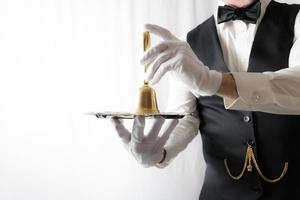 maggiordomo o Cameriere nel nero veste e bianca guanti Tenere oro campana su argento servendo vassoio. concetto di servizio industria e professionale ospitalità. foto