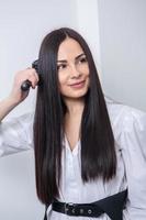 giovane donna pettinatura sua lungo buio capelli con un' pettine nel un' bellezza salone foto