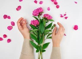 Due mani di un' giovane ragazza con liscio pelle e un' mazzo di rosso peonie foto