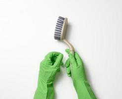 mano nel un' verde gomma da cancellare pulizia guanto detiene un' plastica spazzola su un' bianca sfondo foto