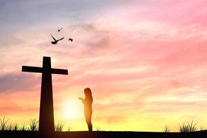 silhouette di persona che prega a una croce al tramonto foto