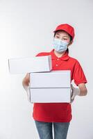 Immagine di un' consapevole giovane consegna uomo nel rosso berretto vuoto maglietta uniforme viso maschera guanti in piedi con vuoto bianca cartone scatola isolato su leggero grigio sfondo studio foto