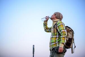 ritratto di escursionista uomo potabile acqua mentre in piedi su montagne con zaino foto