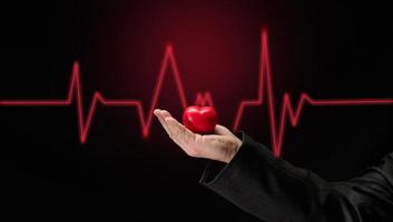 maschio mano Tenere un' rosso cuore su un' buio sfondo, presto diagnosi di il cardiovascolare sistema foto