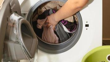 primo piano della mano di una donna che mette i vestiti sporchi nella lavatrice. foto