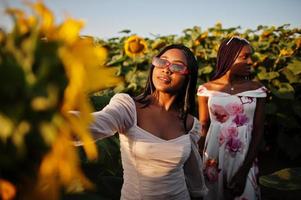 due piuttosto giovani amici neri donna indossano abiti estivi posano in un campo di girasoli. foto