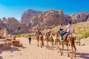I turisti a cavallo di cammelli a petra, giordania, 2018 foto
