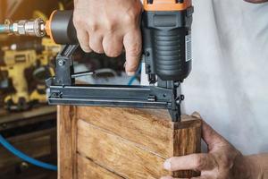 falegname che utilizza la pistola sparachiodi o lo strumento chiodatrice Brad su scatola di legno in un'officina, concetto di lavorazione del legno per il restauro di mobili. messa a fuoco selettiva foto