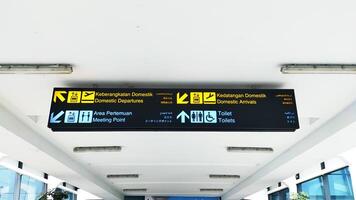 cartello direzione a il indonesiano aeroporto, tradurre nel inglese domestico Partenze, domestico Arrivi, incontro punto, e servizi igienici. foto