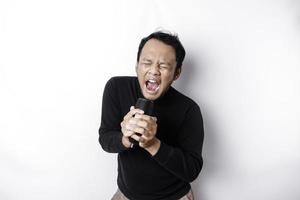 ritratto di spensierato asiatico uomo, avendo divertimento karaoke, cantando nel microfono mentre in piedi al di sopra di bianca sfondo foto