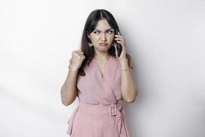 un' insoddisfatto giovane asiatico donna vestito nel rosa, sembra scontento con irritata viso espressioni Tenere sua Telefono foto