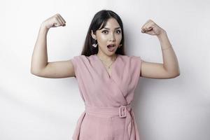 eccitato asiatico donna indossare un' rosa camicetta mostrando forte gesto di sollevamento sua braccia e muscoli sorridente con orgoglio foto
