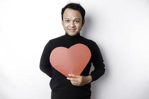 un' ritratto di un' contento asiatico uomo indossare un' nero camicia, Tenere un' rosso a forma di cuore carta isolato di bianca sfondo foto