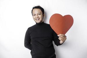 un' ritratto di un' contento asiatico uomo indossare un' nero camicia, Tenere un' rosso a forma di cuore carta isolato di bianca sfondo foto