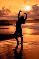 un asiatico donna nel silhouette è fare ginnastica movimenti molto agile su il spiaggia sabbia foto