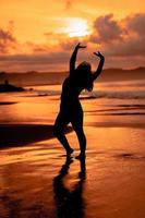 un asiatico donna nel silhouette è fare ginnastica movimenti molto agile su il spiaggia sabbia foto
