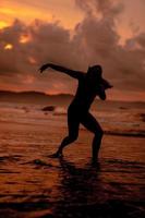 silhouette di un asiatico donna giocando nel il acqua su il spiaggia con forte onde Crashing foto