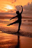 silhouette di un' molto snello ballerina fare balletto pratica solo su il riva del mare con onde Crashing a sua foto