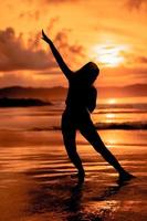 il silhouette di un asiatico adolescente con un' alto corpo è danza balletto su il onde su il spiaggia foto