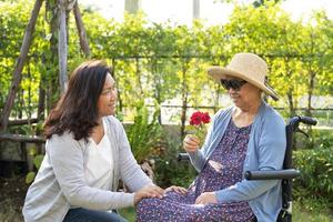 donna anziana asiatica o anziana che tiene fiore di rosa rossa, sorriso e felice nel giardino soleggiato. foto