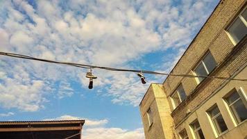 sospeso scarpe da ginnastica su elettrico filo su blu cielo sfondo con bianca nuvole e visibile giallo edificio superiore foto