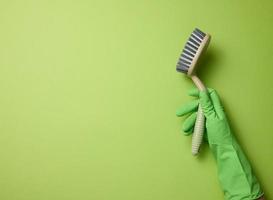 mano nel un' verde gomma da cancellare guanto detiene un' plastica pulizia spazzola su un' verde sfondo foto