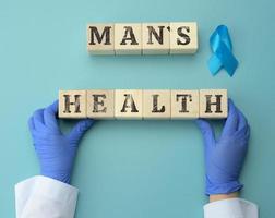 di legno cubi con il iscrizione dell'uomo Salute e Due mani di un' medico nel blu guanti. concetto per tempestivo diagnosi di prostata cancro nel uomini foto