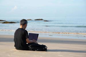 un' anziano adulto utilizzando computer su il spiaggia foto