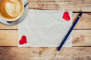 vecchio carta e rosso cuore, caffè tazza con matita su legna sfondo per San Valentino saluto carta. foto