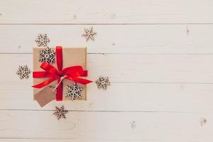 Marrone regalo scatola e i fiocchi di neve su bianca di legno sfondo. Vintage ▾ regalo scatola su di legno sfondo. regalo scatola con rosso nastro su legna sfondo con spazio. foto