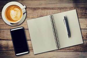 superiore Visualizza taccuino, penna, caffè tazza, e Telefono su legna tavolo, Vintage ▾ filtro. foto
