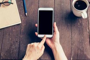 vicino su di donna mano Tenere Telefono con vuoto copia spazio schermo per il tuo pubblicità. mano donna utilizzando Telefono nel caffè negozio. foto