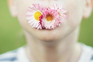 uomo con un' margherita fiore su un' verde sfondo chiudere. bambino bocca con fiore su erba sfondo foto