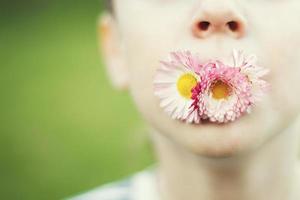 uomo con un' margherita fiore su un' verde sfondo chiudere. bambino bocca con fiore su erba sfondo foto