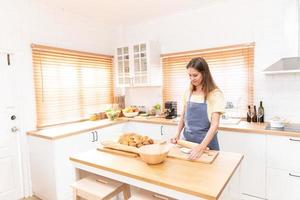 giovane donna opera con di legno rullo perno fabbricazione dolce torta o Pasticcino Impasto nel cucina, contento del Millennio femmina amorevole cucinando. foto