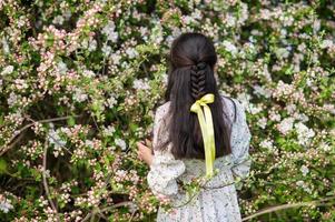 un' giovane ragazza trasformato sua indietro vicino un' fioritura ciliegia albero foto