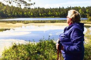 donna anziana con bastoncini nordici in piedi vicino al lago fiorito in primavera all'aperto nella foresta. parco regionale kurtuvenai in lituania foto