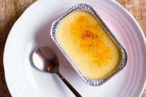 francese creme brulee nel un' Foglio tazza su il bianca piatto, con il cucchiaio su il lato. foto