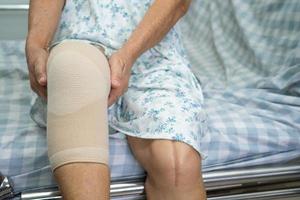 asiatico anziano donna paziente con bendare compressione ginocchio sostegno supporto infortunio su il letto nel ospedale reparto, salutare forte medico concetto. foto