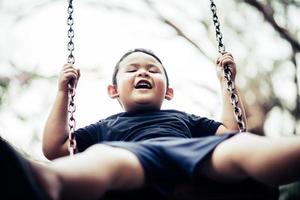 adorabile ragazzino divertendosi su un'altalena all'aperto foto