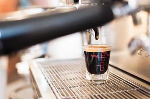 avvicinamento nero caffè nel misurazione tazza mettere su caffè creatore, caffè macchina fabbricazione caffè espresso foto