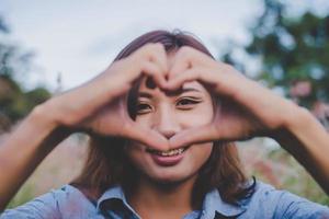 bella donna sorridendo alla telecamera e facendo a forma di cuore con le sue mani foto