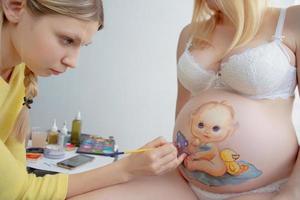 giovane trucco artista disegnare un' bambino piccolo su il pancia foto