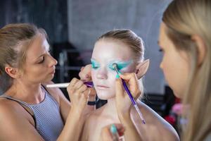 Due donne si applica creativo trucco per il viso di un' carino giovane modello foto