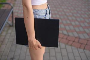 un' ragazza detiene un' il computer portatile nel sua mani contro il sfondo di sua gambe foto